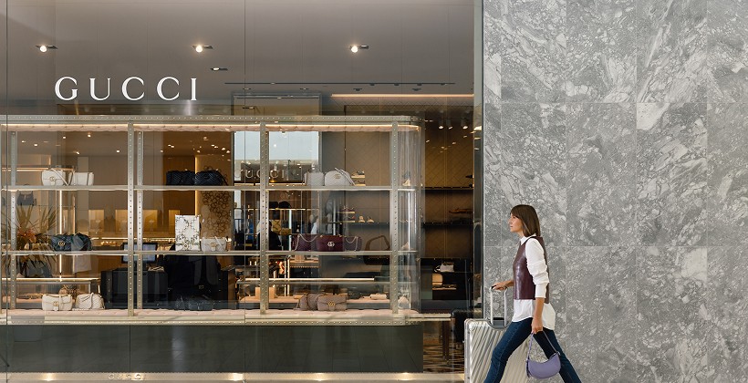 Woman walking past a Gucci store carrying shopping bags inside a busy shopping centre